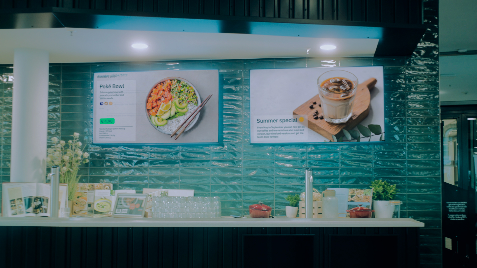 Ein moderner Gastronomiebereich mit Bildern von Pok&eacute;-Bowl und einem Sommerspecial auf blauen Fliesen.