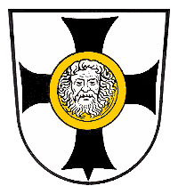 Wappen der Stadt Visselhövede mit schwarzem Kreuz auf weißem Grund und einem goldenen Medaillon mit einem bärtigen Gesicht in der Mitte.