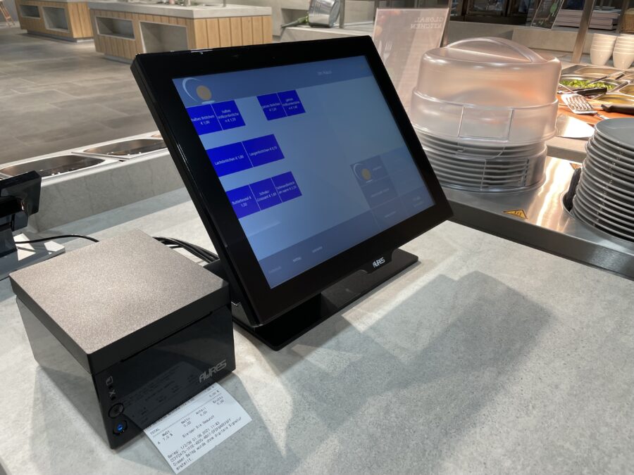 Ein modernes Kassensystem mit Touchscreen und einem kleinen Computer daneben, auf einer Restauranttheke platziert.