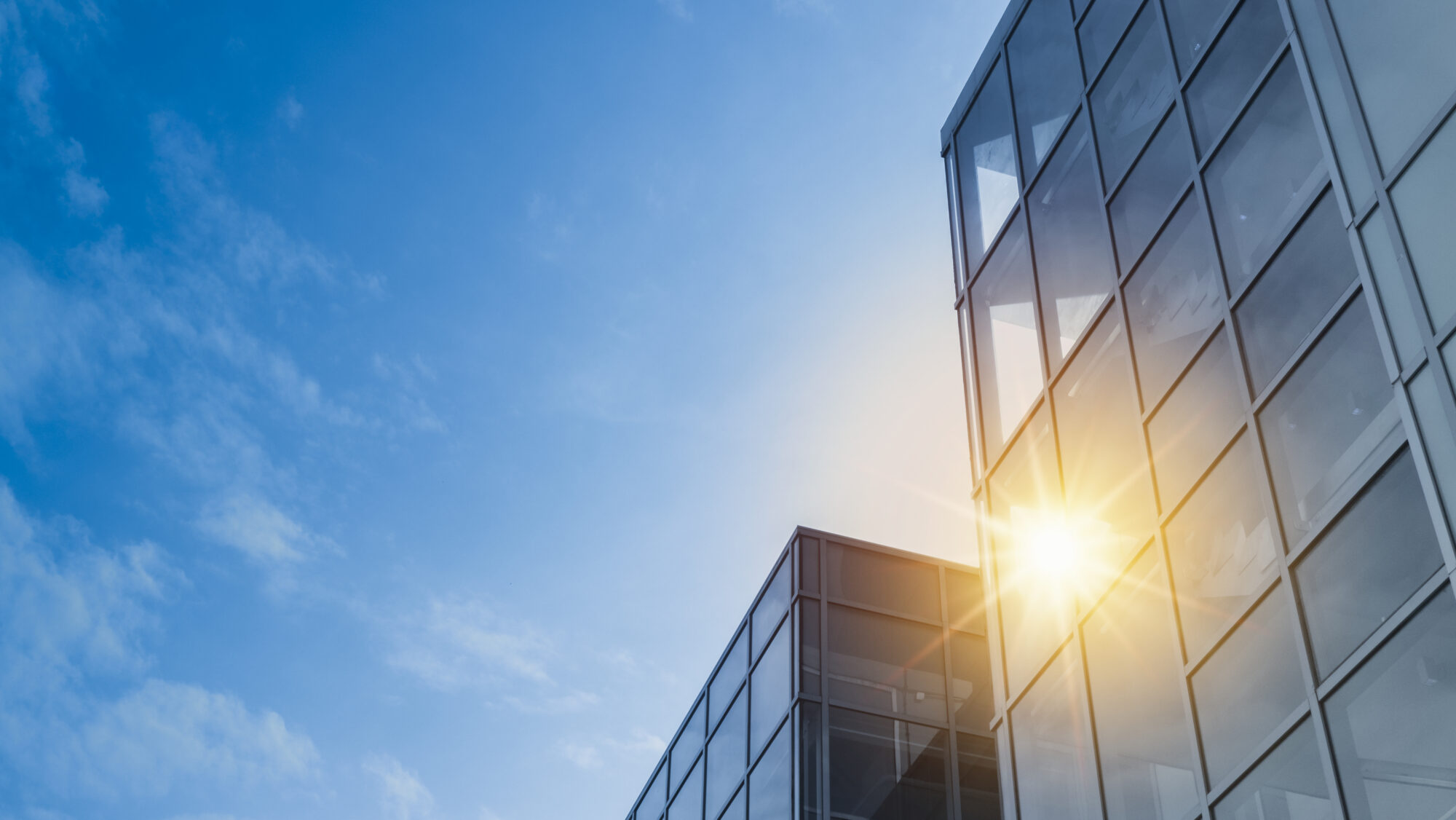 Moderne Geb&auml;ude mit Glasfassade unter klarem Himmel, Sonnenstrahlen reflektieren auf den Fenstern.